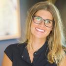 Smiling blonde woman with glasses, black top, warm indoor photo